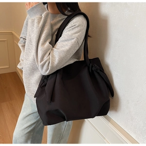 Side view of black minimalist tote bag with knot detail worn by a model in interior setting