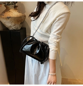 Detail of glossy black patent leather bucket bag with silver chain and white logo