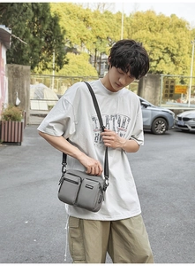 Outdoor street scene showing grey nylon crossbody bag with multi-pocket design on model