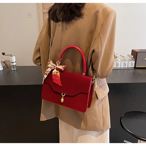 Detail of red suede bridal handbag with gold chain strap and decorative silk scarf wrap