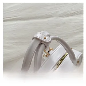 Close-up of white quilted handbag featuring round handles and golden metal zipper details
