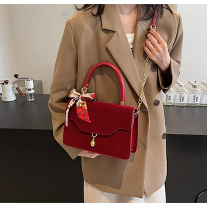 Detail of red velvet handbag with gold droplet pendant and decorative silk scarf