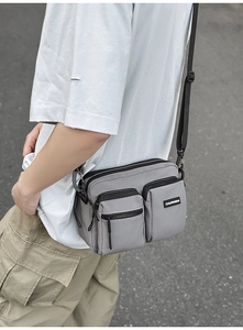 Macro detail of multi-pocket nylon crossbody bag showing zippers and durable gray fabric