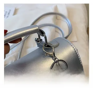 Détail du sac argenté avec fermoir mousqueton brillant et pompon rose en peluche