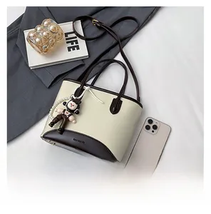 Détail du sac bicolore avec breloque perle et accessoire poupée sur une surface blanche