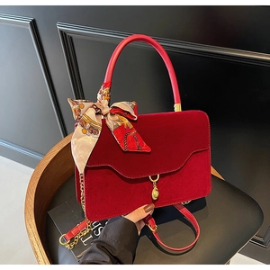 Macro shot of red velvet handbag featuring a gold pendant, chain strap, and silk scarf detail