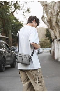 Detail of grey multi-pocket nylon messenger bag showing durable zippers and brand logo