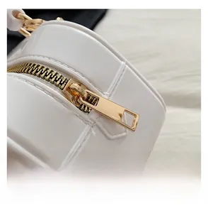 Detail of smooth gold zipper and metallic chain on white quilted leather handbag