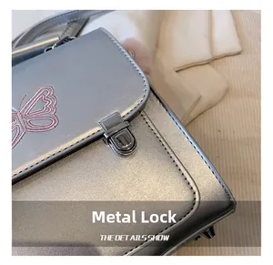 Gros plan du sac argenté avec broderie papillon rose et fermoir métallique brillant