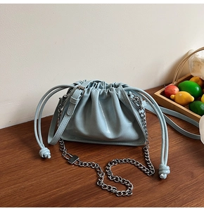 Detail of light blue pleated cloud bag with silver chain strap on a wooden table