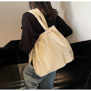 Detail view of cream tote bag featuring a decorative knotted strap and spacious canvas body