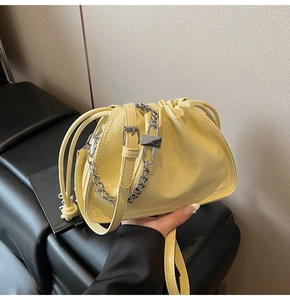 Detail of light yellow drawstring bucket bag with silver chunky chain and leather strap
