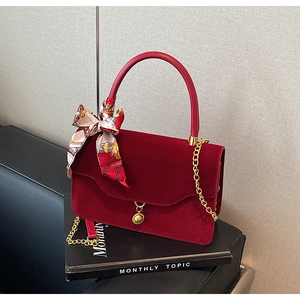 Detail of burgundy velvet handbag with round handle, gold chain and floral scarf accessory