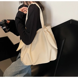 Detail view of a beige minimalist tote bag featuring a large decorative side bow knot