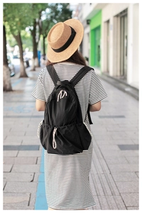 Detail of black nylon backpack featuring white woven zipper pulls and side pockets