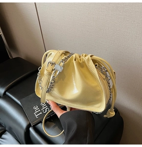 Detail of yellow glossy patent leather bucket bag with silver chain strap and drawstring