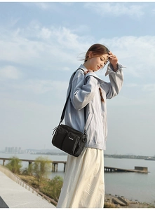 Outdoor shot of a black crossbody bag with multiple zip pockets and adjustable strap