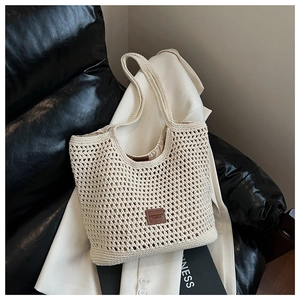 Detail of cream crochet tote bag featuring a leather logo patch on a woven grid surface