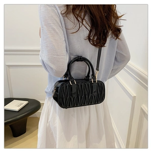 Side view of a black matelassé cylinder bag with gold hardware worn as a crossbody