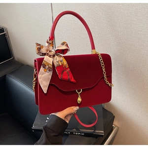 Close-up of red velvet bridal handbag with gold chain, metal ring detail, and floral scarf