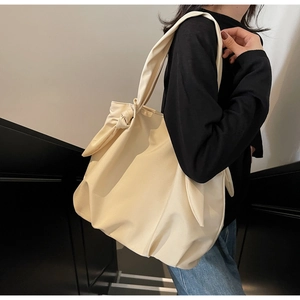 Detail of a large beige tote bag featuring a decorative bow knot on the shoulder strap