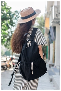 Rear view of a black lightweight backpack with striped drawstrings on a female model