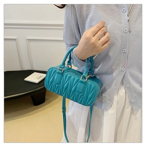 Detail shot of a turquoise pleated patent leather handbag with gold-tone metal hardware