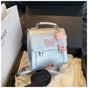 Gros plan d'un mini sac à dos argenté avec broderie papillon rose en coffret