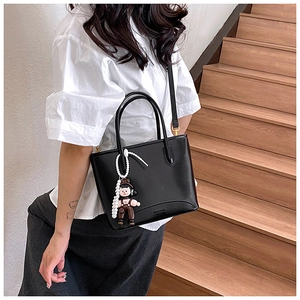 Détail d'un sac seau noir mat avec une breloque de poupée mignonne et une chaîne de perles