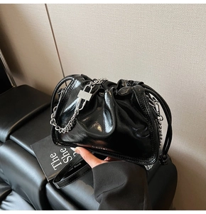 Detail of black glossy drawstring bucket bag with silver chunky chain and lock pendant