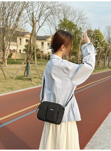 Outdoor lifestyle shot of black nylon crossbody bag with dual zipper pockets and strap
