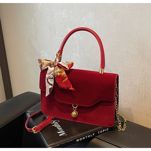 Close-up of burgundy velvet wedding handbag with golden pendant and floral scarf detail