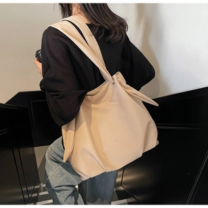 Detail view of a beige oversized canvas tote bag with wide shoulder strap on a model