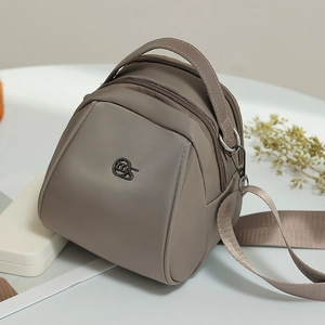 Detail view of taupe triangular crossbody bag with three zipper compartments and logo