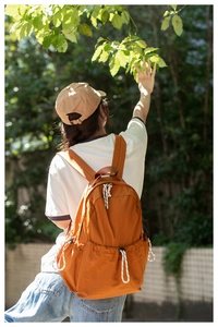 Outdoor view of a waterproof caramel orange backpack with drawstring side pockets and dual straps