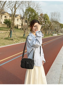 Detail of black nylon crossbody bag featuring multiple zipper pockets and logo on track