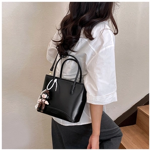 Détail d'un sac seau chic en cuir noir avec un joli pendentif en forme de poupée