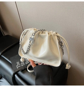 Close-up of cream white glossy bucket bag featuring chic silver chain and drawstring details