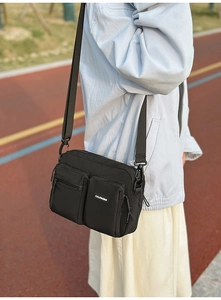 Detail view of the black crossbody bag showing multiple functional zipper pockets and nylon fabric