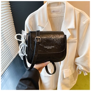 Détail du sac bandoulière en similicuir plissé noir avec breloque nœud en dentelle