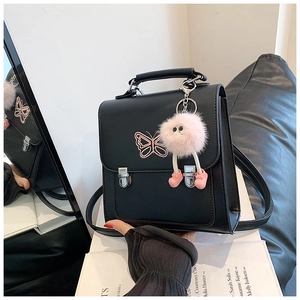 Détail du sac à dos en similicuir noir avec broderie papillon rose et breloque pelucheuse