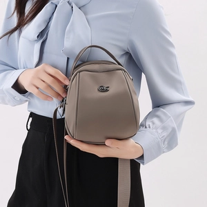 Detail view of a compact shell bag in matte taupe nylon with wide woven shoulder strap