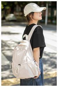 Side view of model wearing lightweight cream backpack with drawstring side pockets