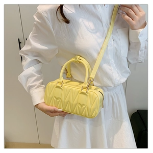 Detail view of bright yellow quilted cylinder bag with gold hardware and shoulder strap