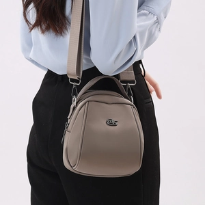 Detail of taupe mini shell crossbody bag with adjustable wide strap and circular logo
