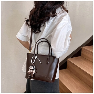 Détail du sac cabas en cuir marron brillant avec charm poupée sur un escalier