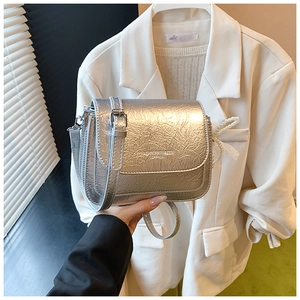 Détail du sac bandoulière argenté avec breloque nœud en dentelle perlée et logo mode