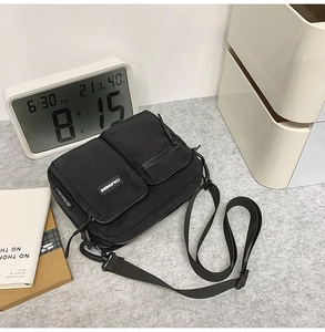 Detail of black nylon crossbody bag featuring multiple zippers and adjustable strap