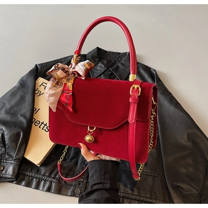 Detail of red bridal handbag featuring gold medallion charm and silk scarf handle wrap