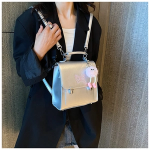 Détail du sac à dos argenté avec broderie papillon rose et breloque peluche sur le mannequin